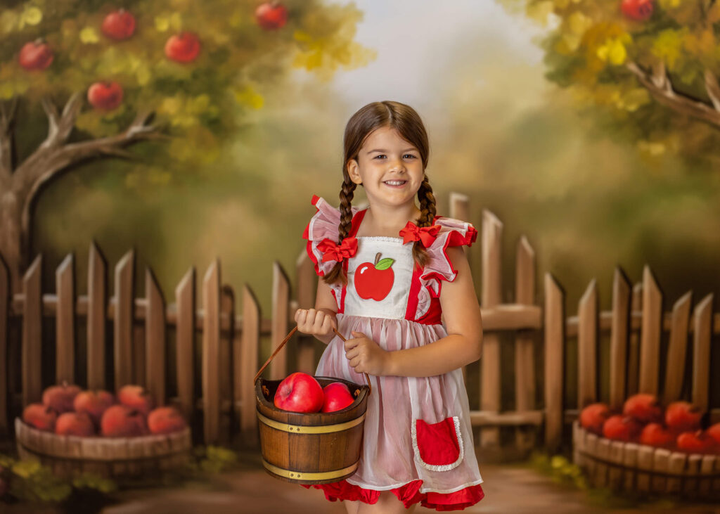 A little girl in a red apple dress is apple picking with a basket of apples
