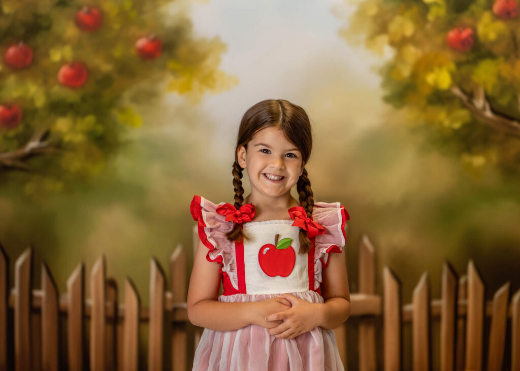 A little girl in a red apple dress is posing and smiling